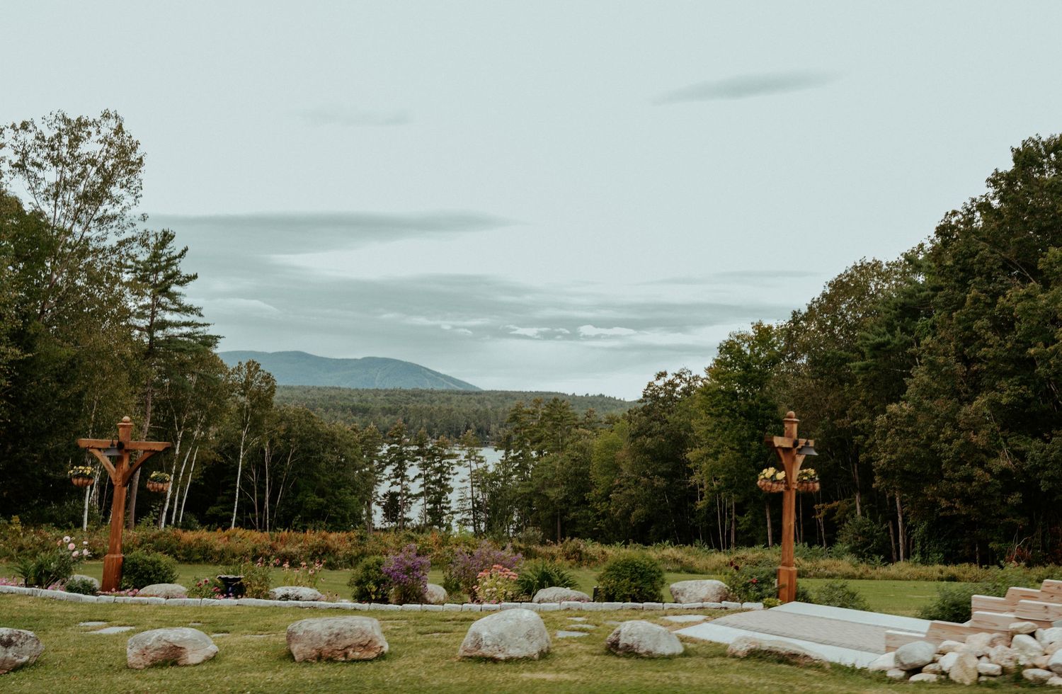 Outdoor wedding ceremony setup with wooden cross decorations on a green lawn overlooking a serene lake and mountain landscape.