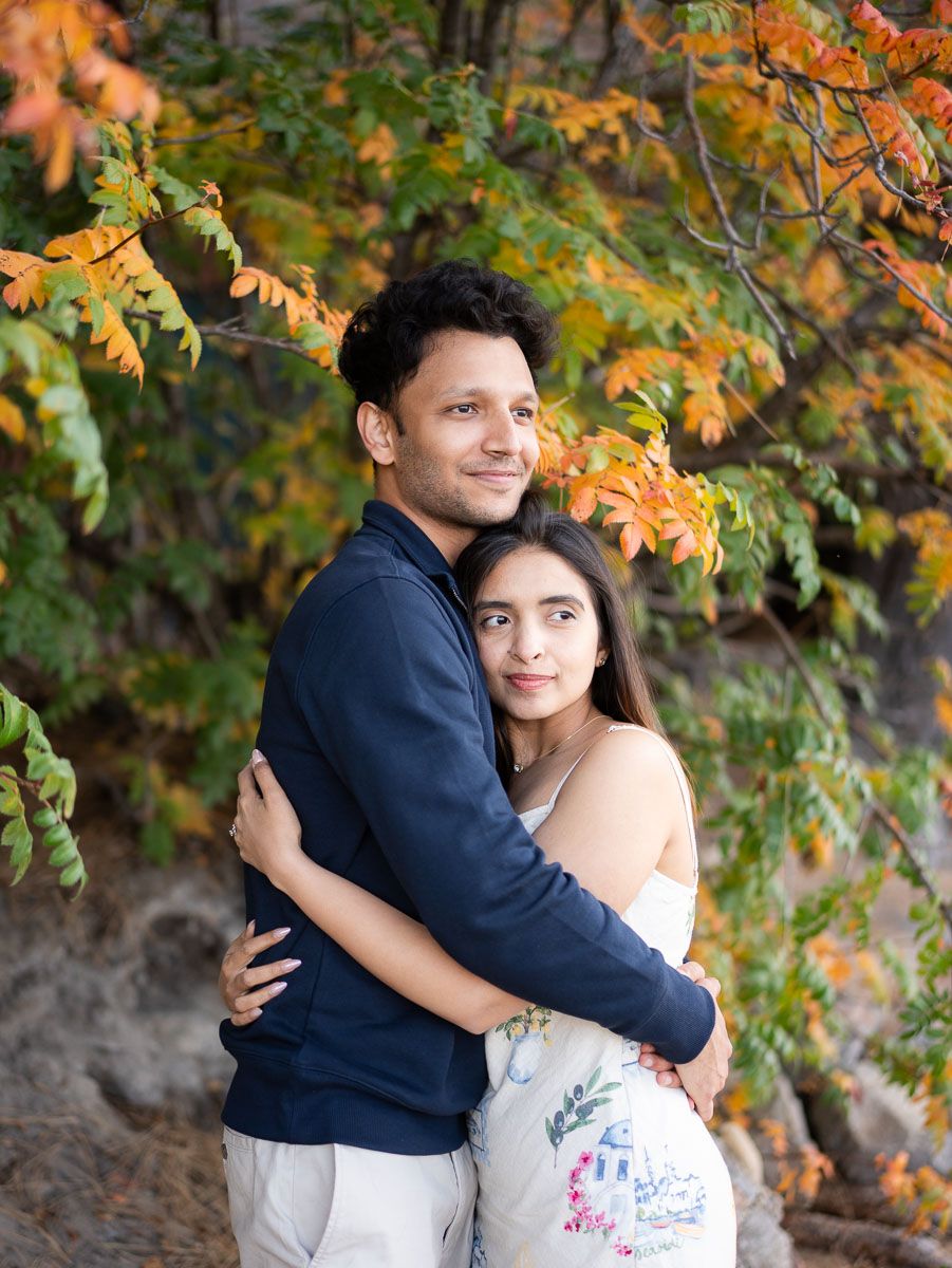 Couple embracing outdoors under colorful autumn foliage with orange and green leaves in fall season.