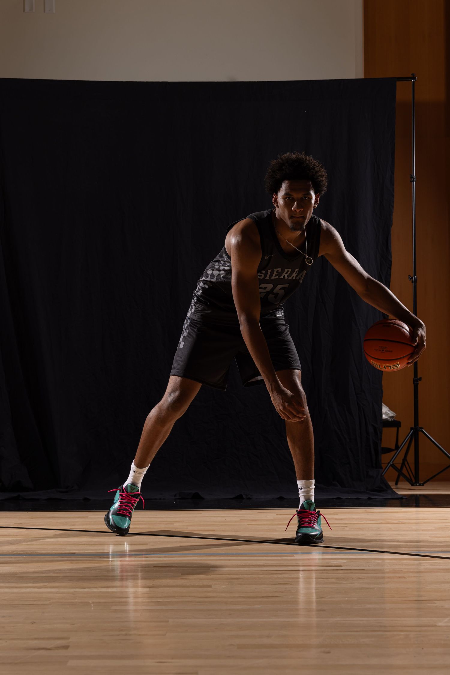 Basketball player in Sierra jersey dribbling on hardwood court against dark backdrop in professional photo shoot.