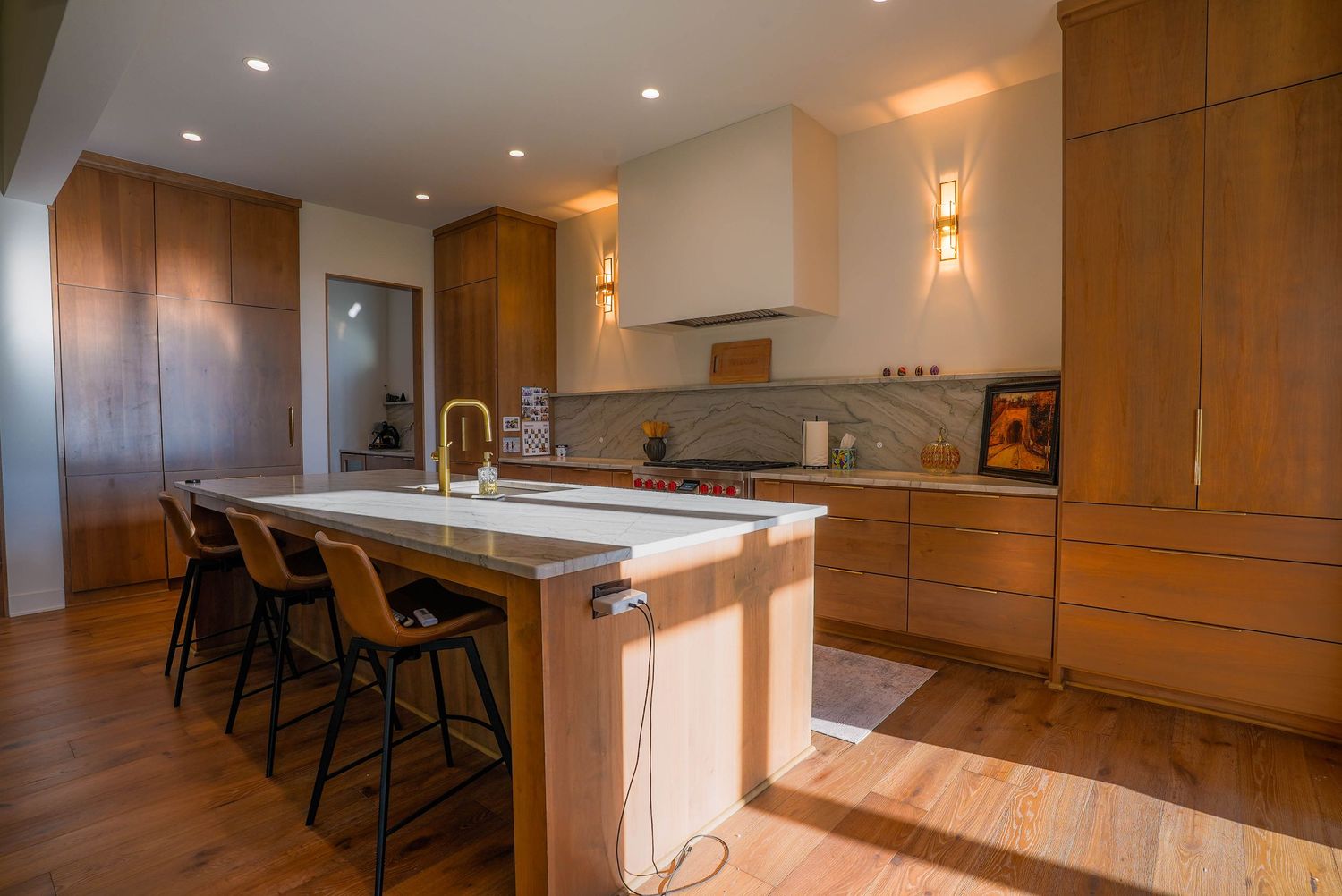 Modern kitchen with wood cabinets, white island, bar stools, and hardwood floors in an open-concept layout.