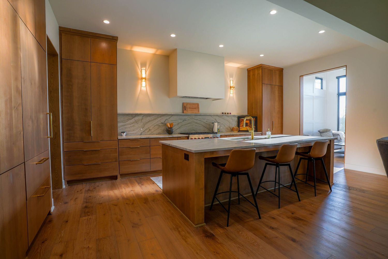 Modern kitchen with warm wood cabinets, white quartz island, bar stools, marble backsplash, and hardwood floors.