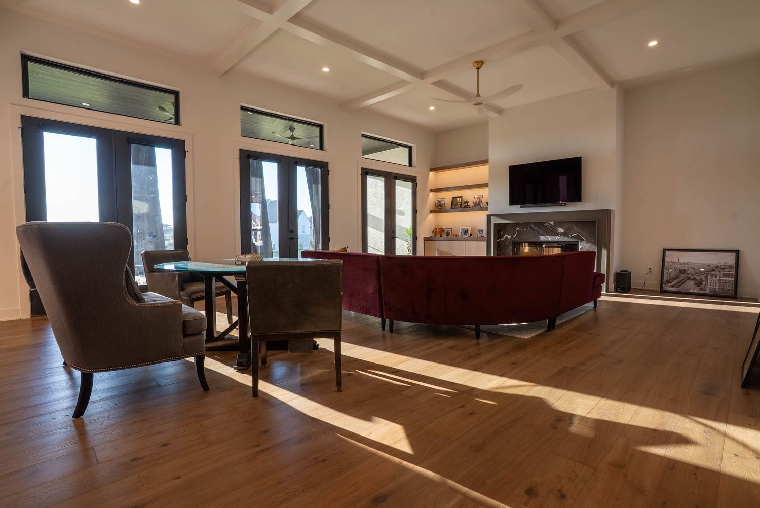 Spacious living room with hardwood floors, gray and red sofas, wall-mounted TV, fireplace, and large windows.