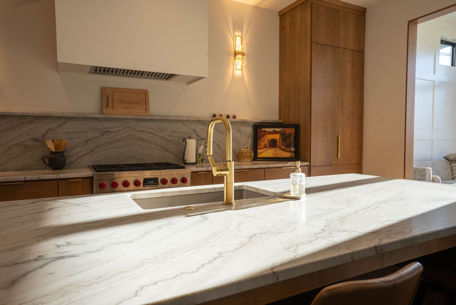 Elegant kitchen with marble waterfall island, gold faucet, stainless range, and warm wood cabinetry.