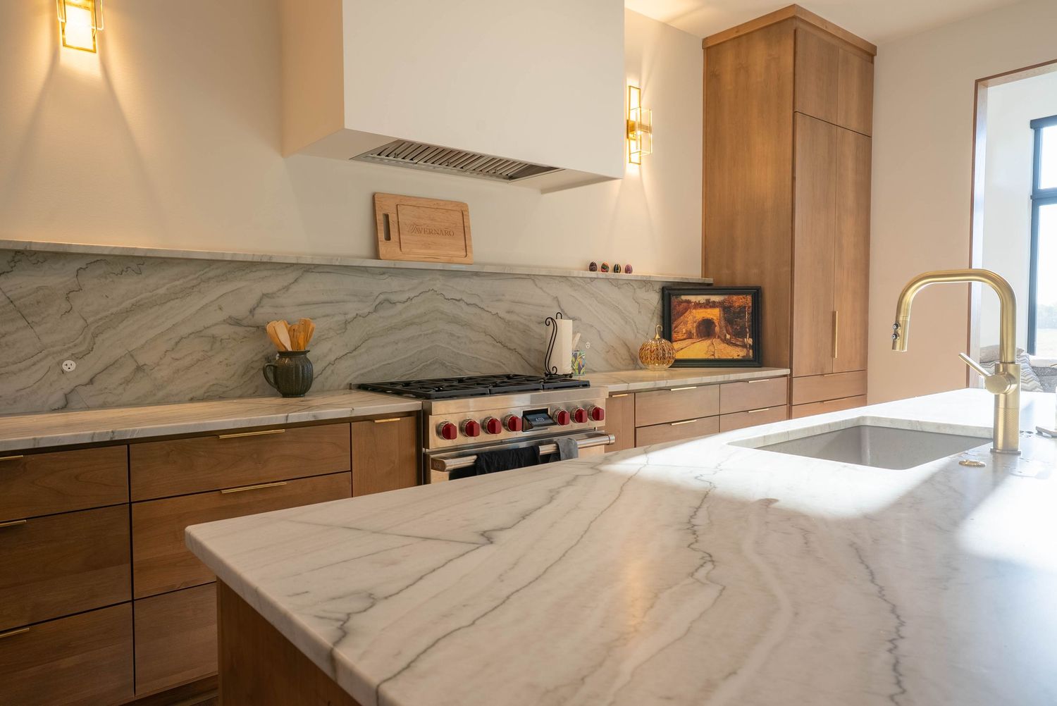 Modern kitchen with marble countertops, wood cabinets, stainless range, and gold faucet sink.
