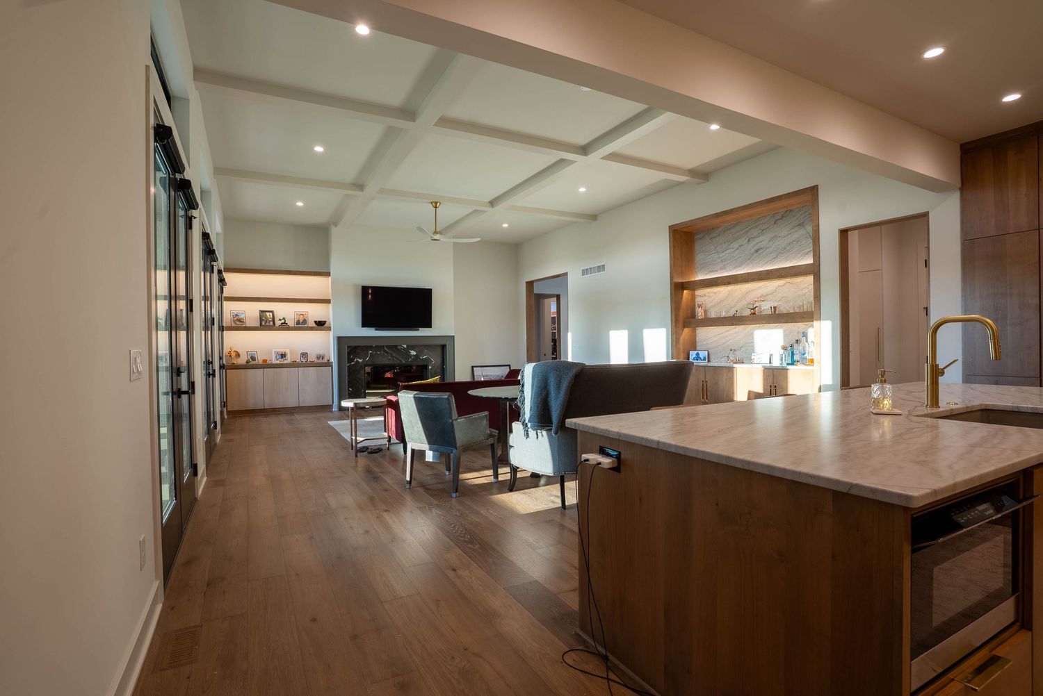 Open-plan kitchen and living area with coffered ceilings, hardwood floors, fireplace, and warm wood cabinetry.