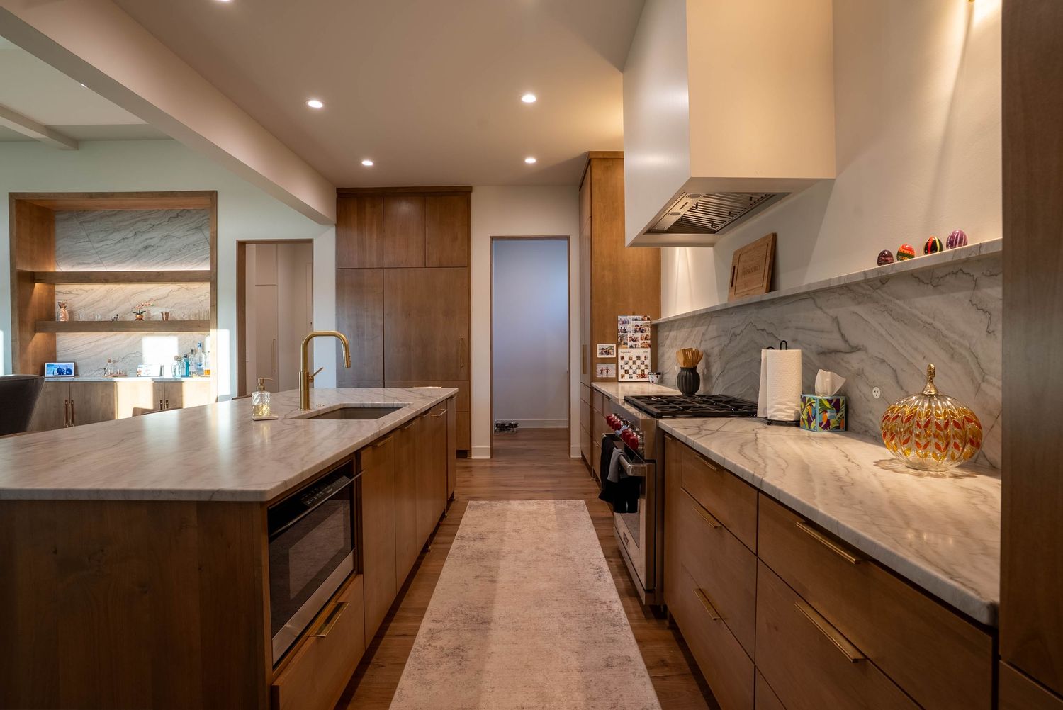 Elegant galley kitchen with wood cabinets, marble backsplash, quartz island countertop, and stainless appliances.