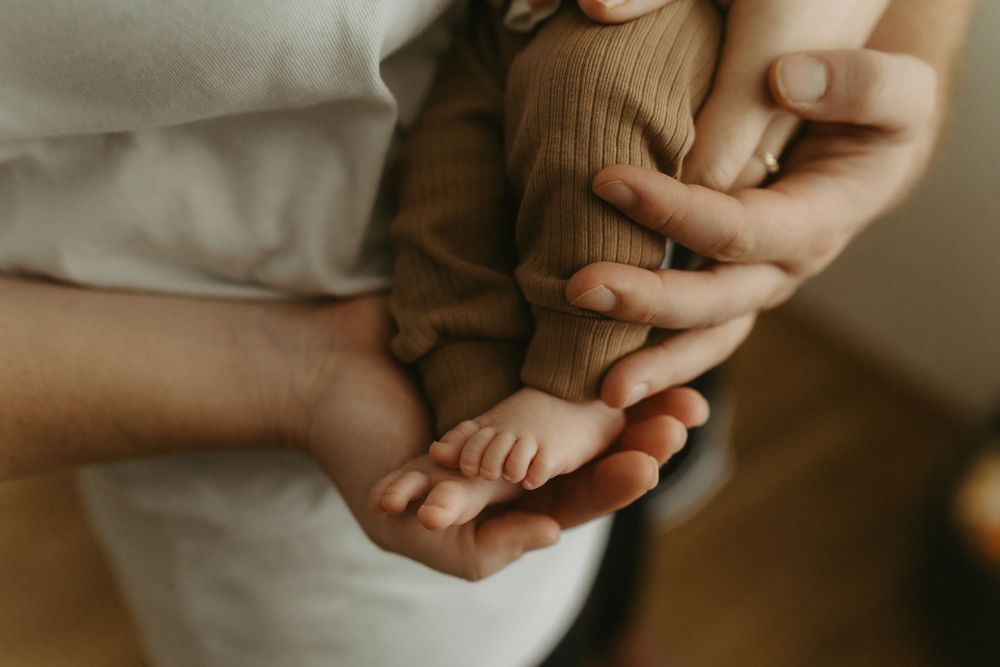 Close-up of parents cradling newborn baby feet in their hands, capturing a tender family bonding moment.