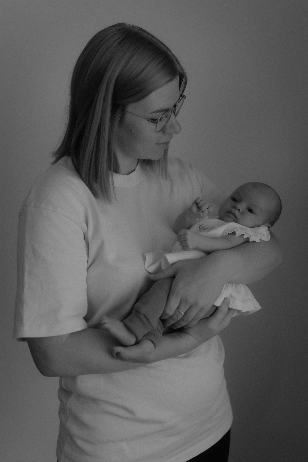Black and white photo of a mother in glasses holding her newborn baby in her arms.