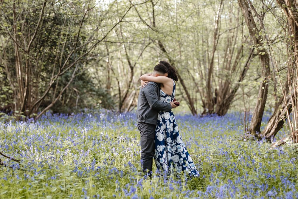 Couple embracing in a bluebell woodland, surrounded by purple wildflowers and trees in bloom.