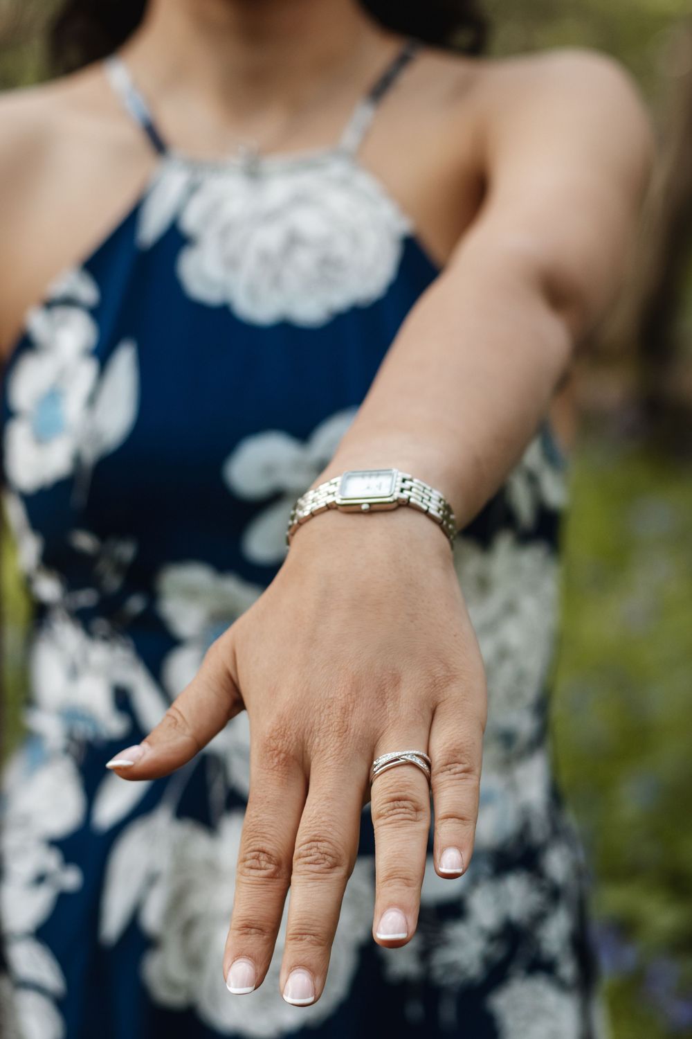 Close-up of engagement ring on womans hand wearing blue floral dress and silver watch.