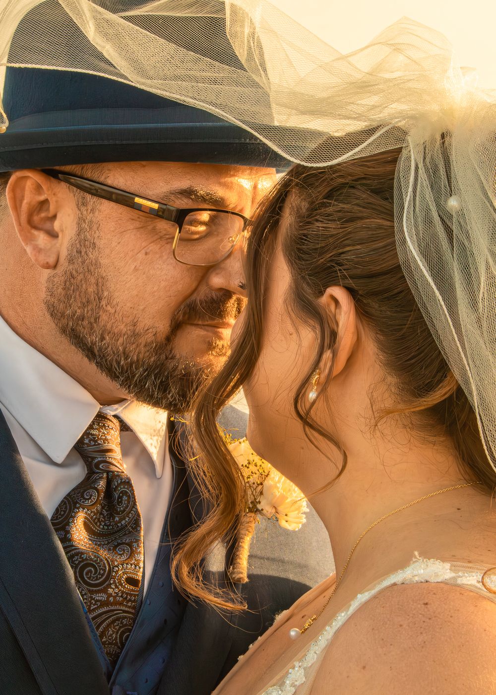 Bride and groom share an intimate moment under a veil, bathed in golden sunset light at their wedding.