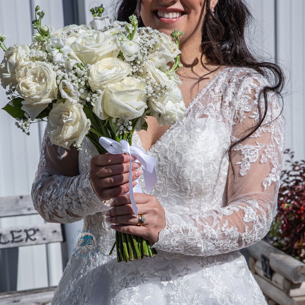 Bride in lace long-sleeve wedding gown holding elegant white rose bouquet with baby's breath on her wedding day.