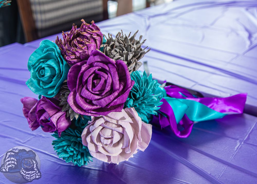 Colorful handmade bouquet of purple, teal, and white paper roses on a purple tablecloth.