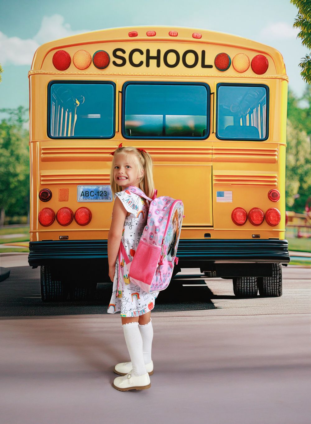Young girl with pink backpack standing in front of yellow school bus.
