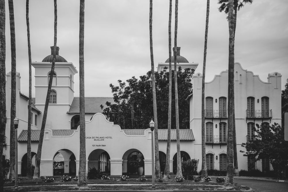 Black and white photo of a Spanish Colonial Revival building with tall palm trees in foreground.