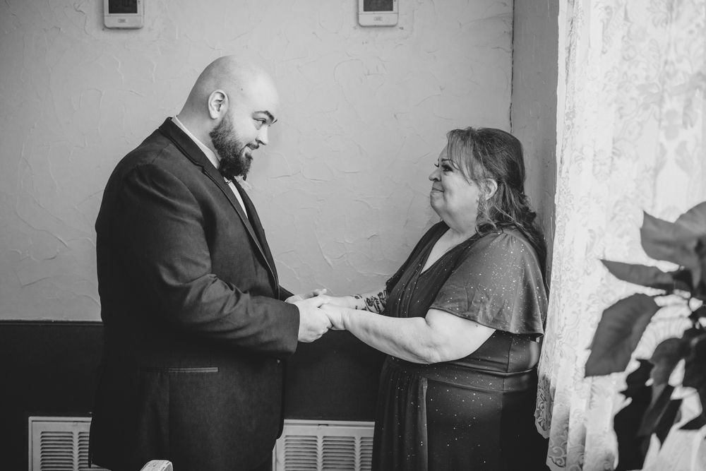 Emotional black and white photo of groom holding hands with family member during intimate wedding preparation moment.