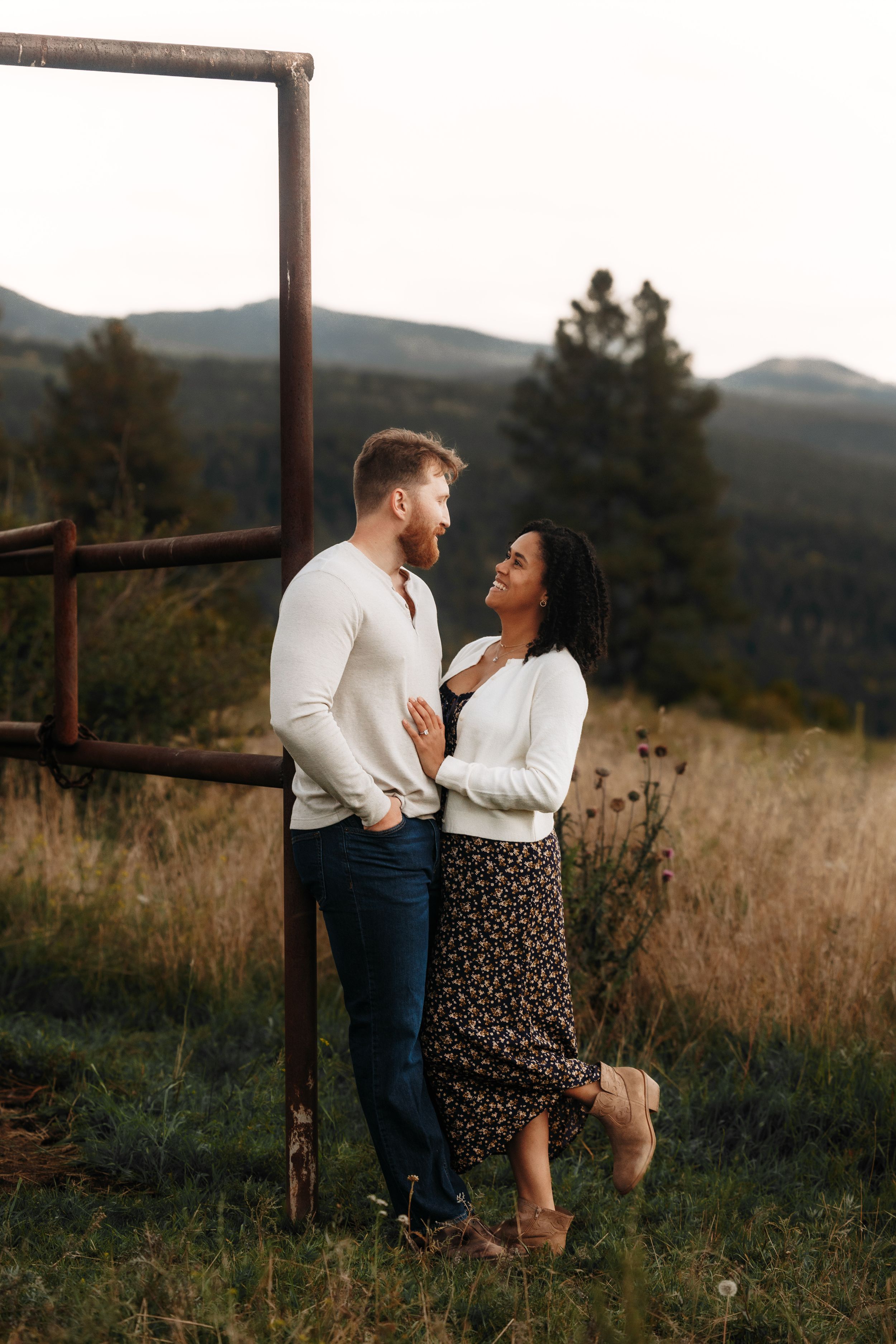 A couple shares a romantic moment in a mountain meadow, the man in white sweater and jeans, woman in floral skirt.