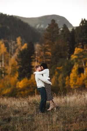 Couple embracing in autumn mountain meadow with golden trees and peaks in background.