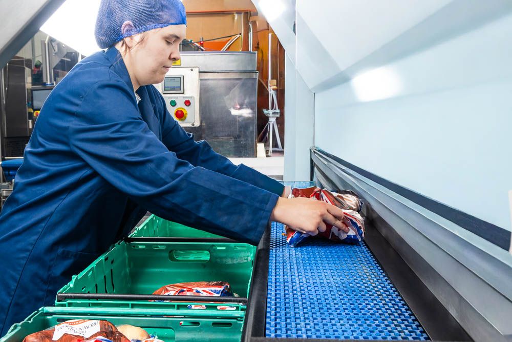 Female factory worker in blue uniform operating machinery in a food processing plant.