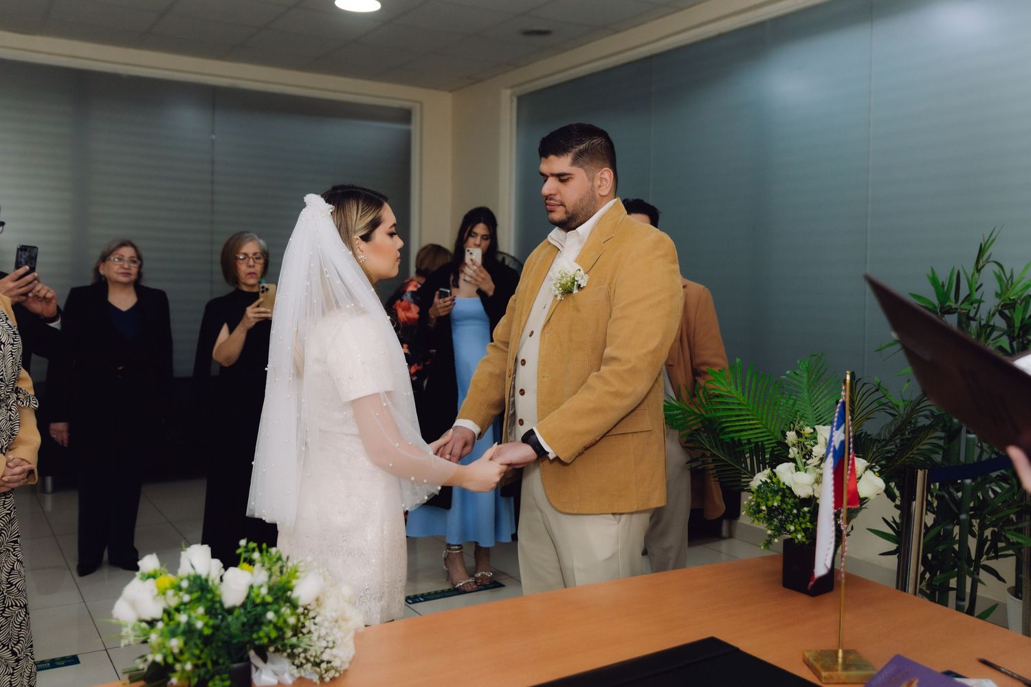Bride and groom exchange vows at civil wedding ceremony while guests watch and photograph the moment.