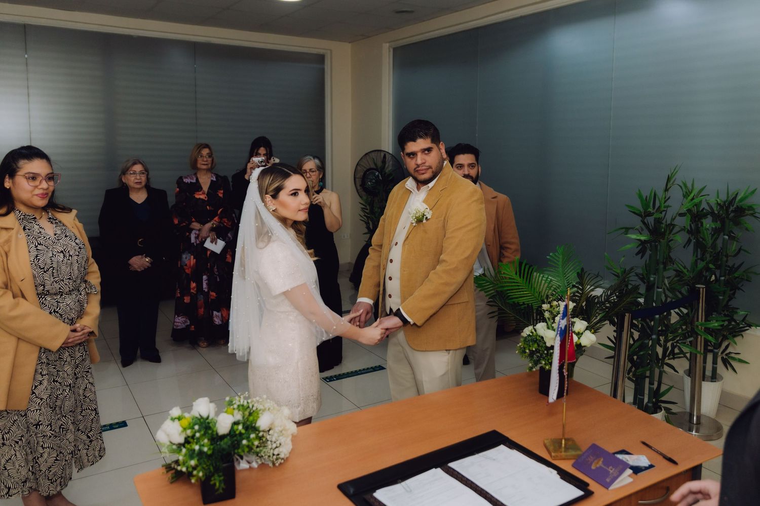 Couple exchanges rings at civil wedding ceremony with guests standing behind them in formal office setting.