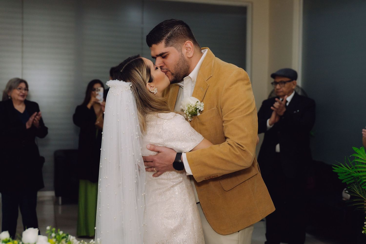 Newlyweds share passionate first kiss as guests applaud at civil wedding ceremony.