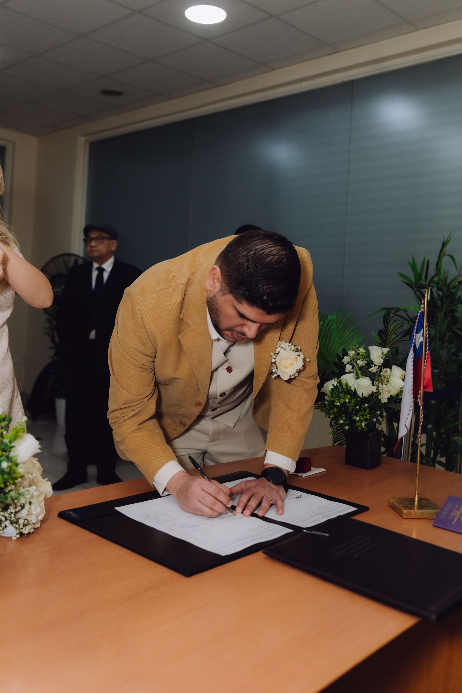Groom in tan suit signing wedding documents at a civil ceremony.