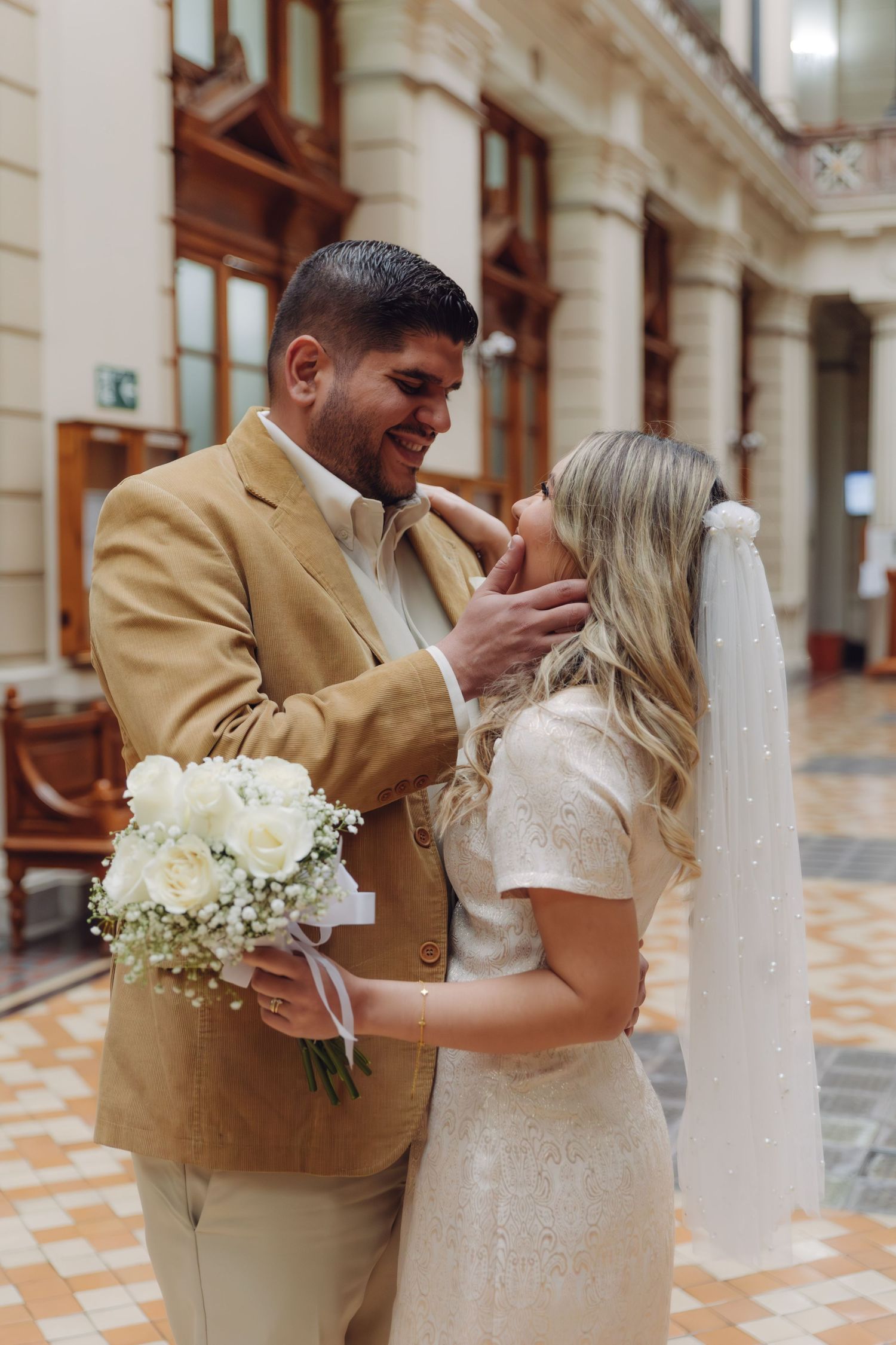 Groom tenderly touching brides face as they share an intimate moment, bride wearing veil and lace dress.