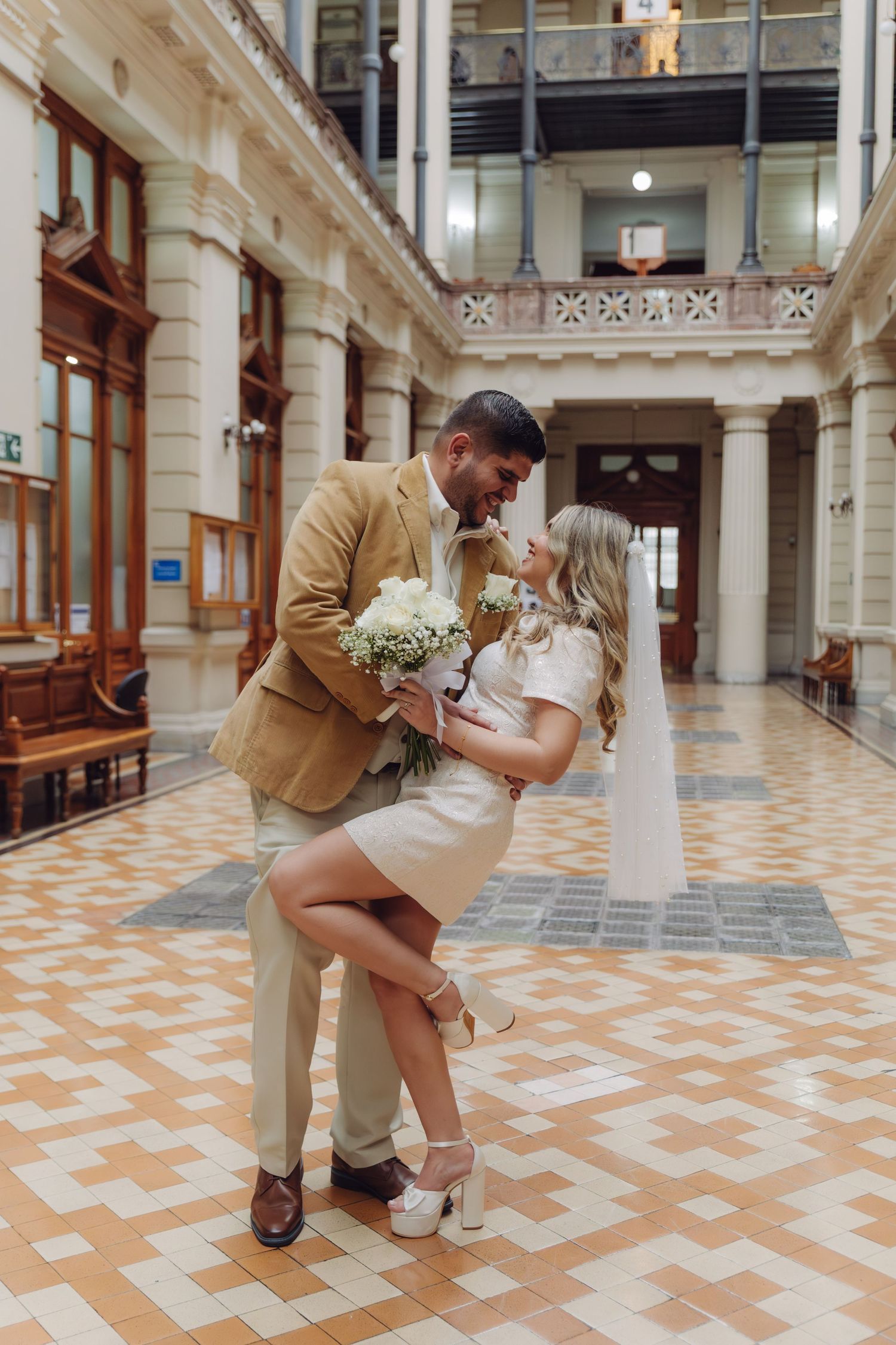 Groom dipping bride in a romantic pose inside a beautiful historic building with ornate architecture.