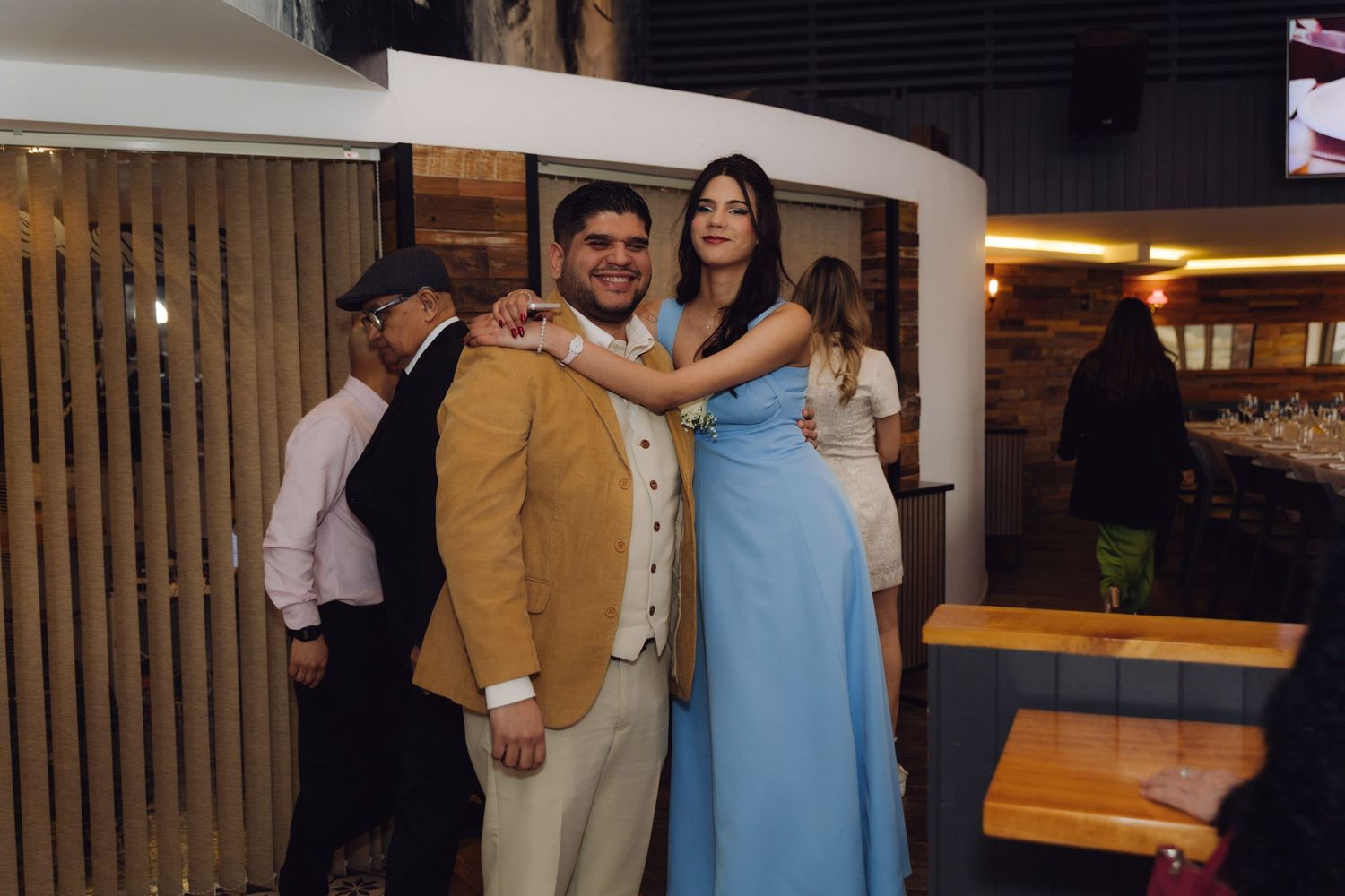 Guest in light blue gown poses with groom in tan suit at relaxed wedding reception venue.