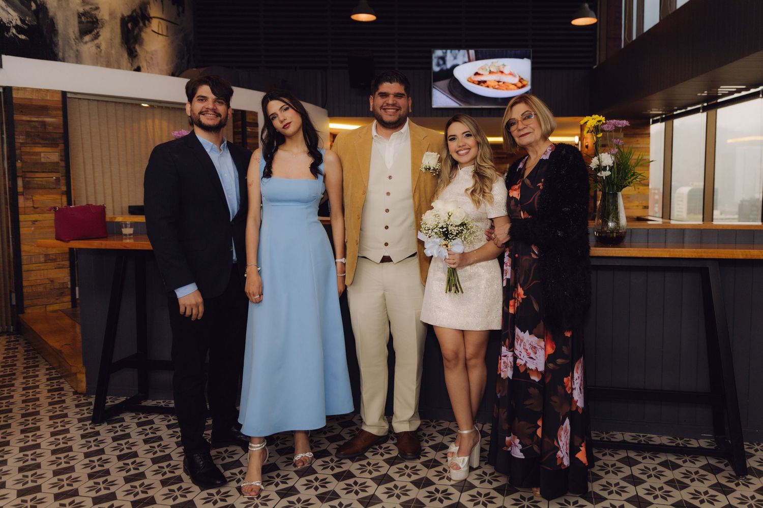 Wedding party of five poses together in casual attire at a modern restaurant reception.