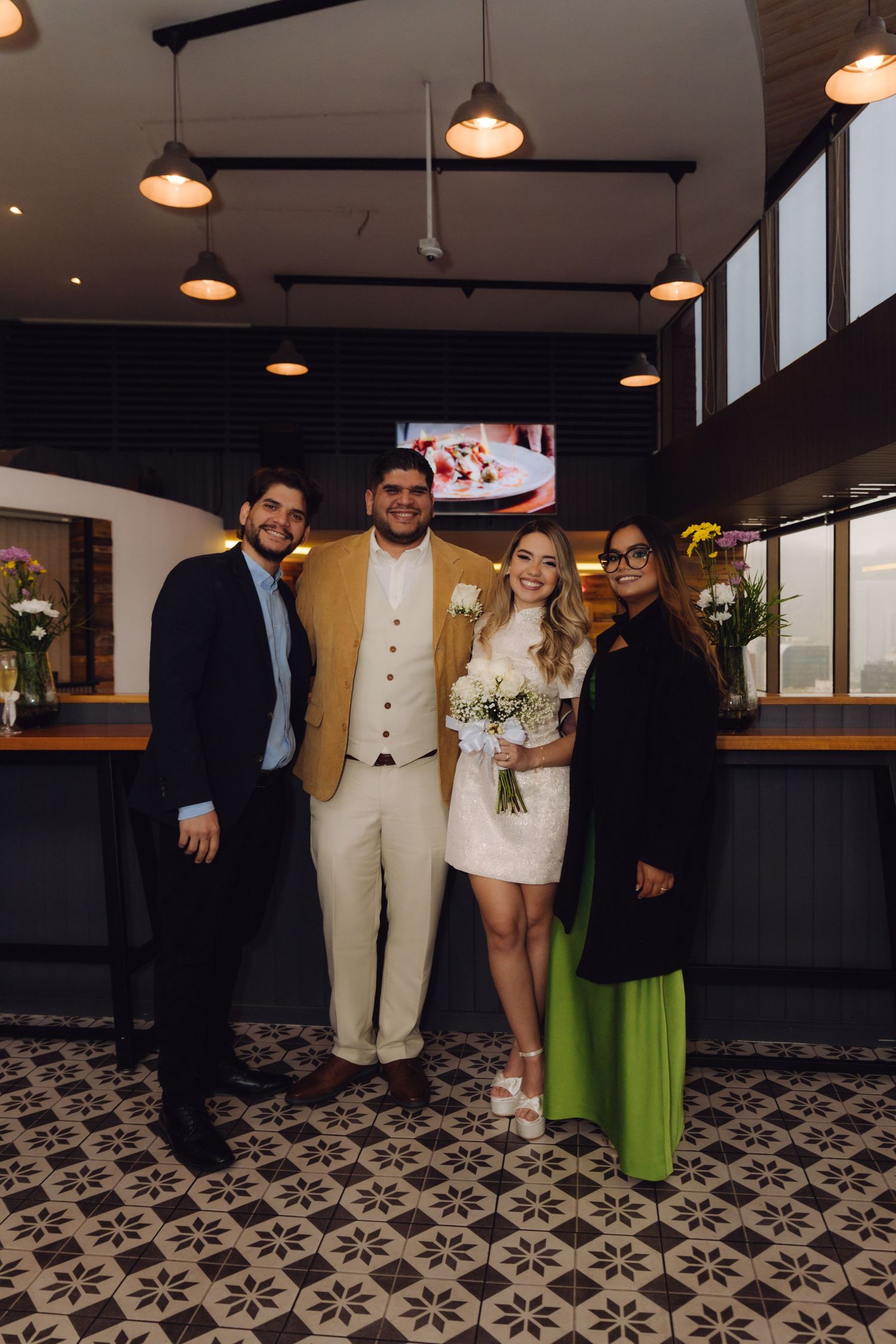 Wedding couple poses with two guests in a warmly lit modern restaurant reception venue.