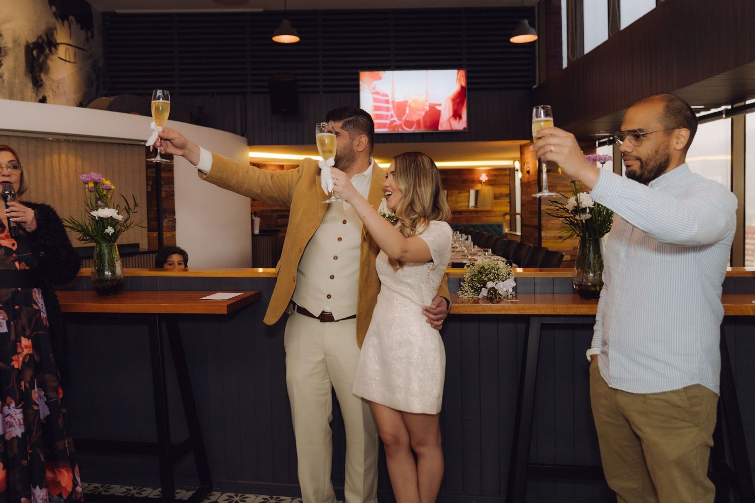 Newlywed couple and guests raising champagne glasses in a celebratory toast at a modern bar setting.