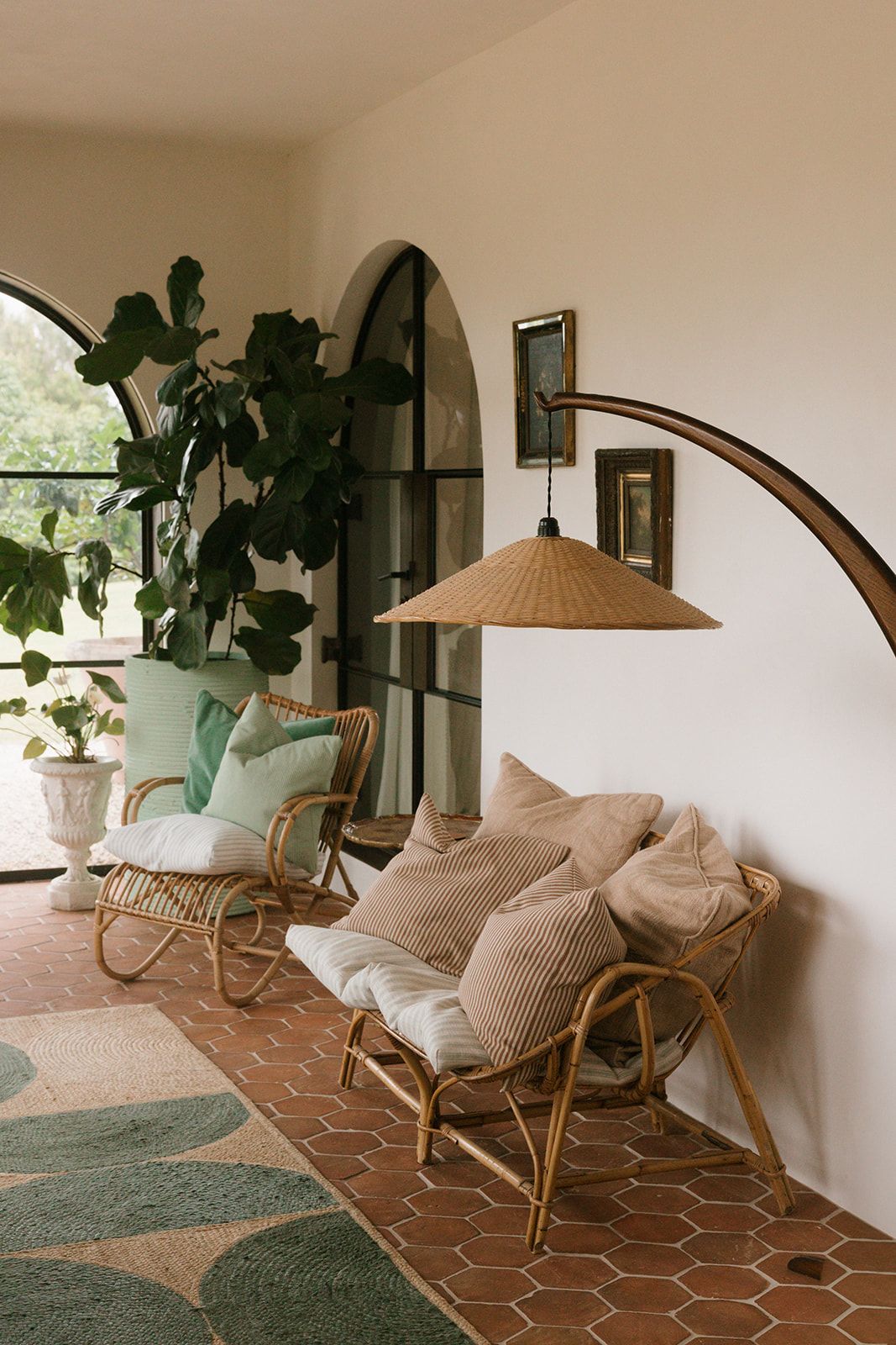 Boho living room with rattan chairs, neutral cushions, arched windows, terracotta tile floor, and a woven arc floor lamp.