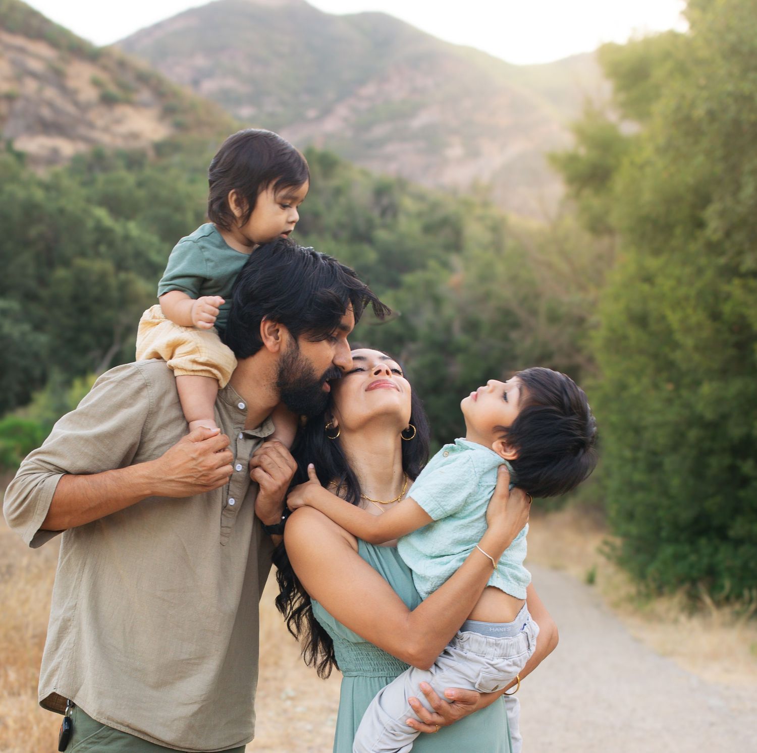 Family of four enjoying a scenic mountain trail, parents lovingly holding two young children outdoors.