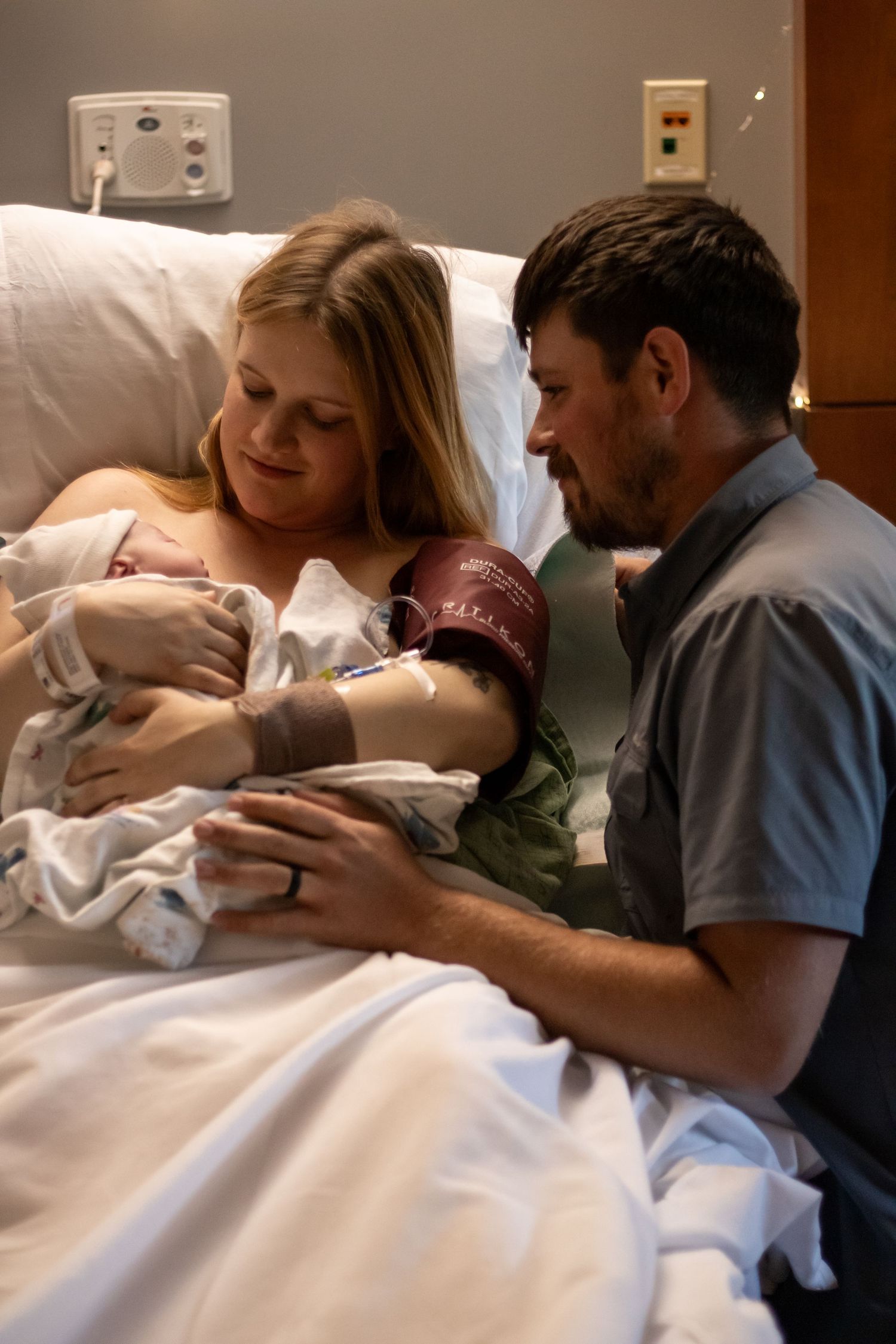 New parents gazing lovingly at their newborn baby in a hospital bed together.