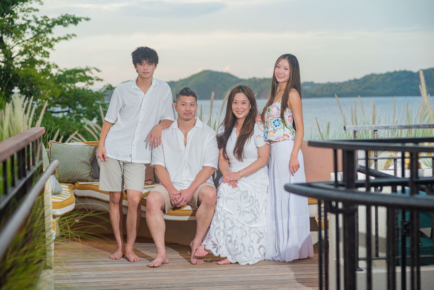 Family of four posing on a waterfront deck at sunset, dressed in white and casual attire.