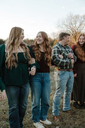 Two smiling young women with red hair walk outdoors during a casual family gathering in a field at golden hour.