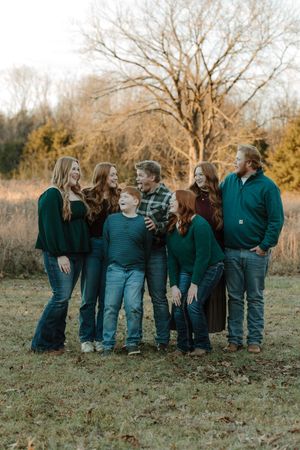 Family of seven laughing together outdoors in green and teal outfits during a fall family portrait session.