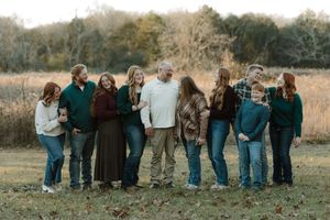 Large family group portrait outdoors in a field during fall, wearing coordinated green and neutral tones.
