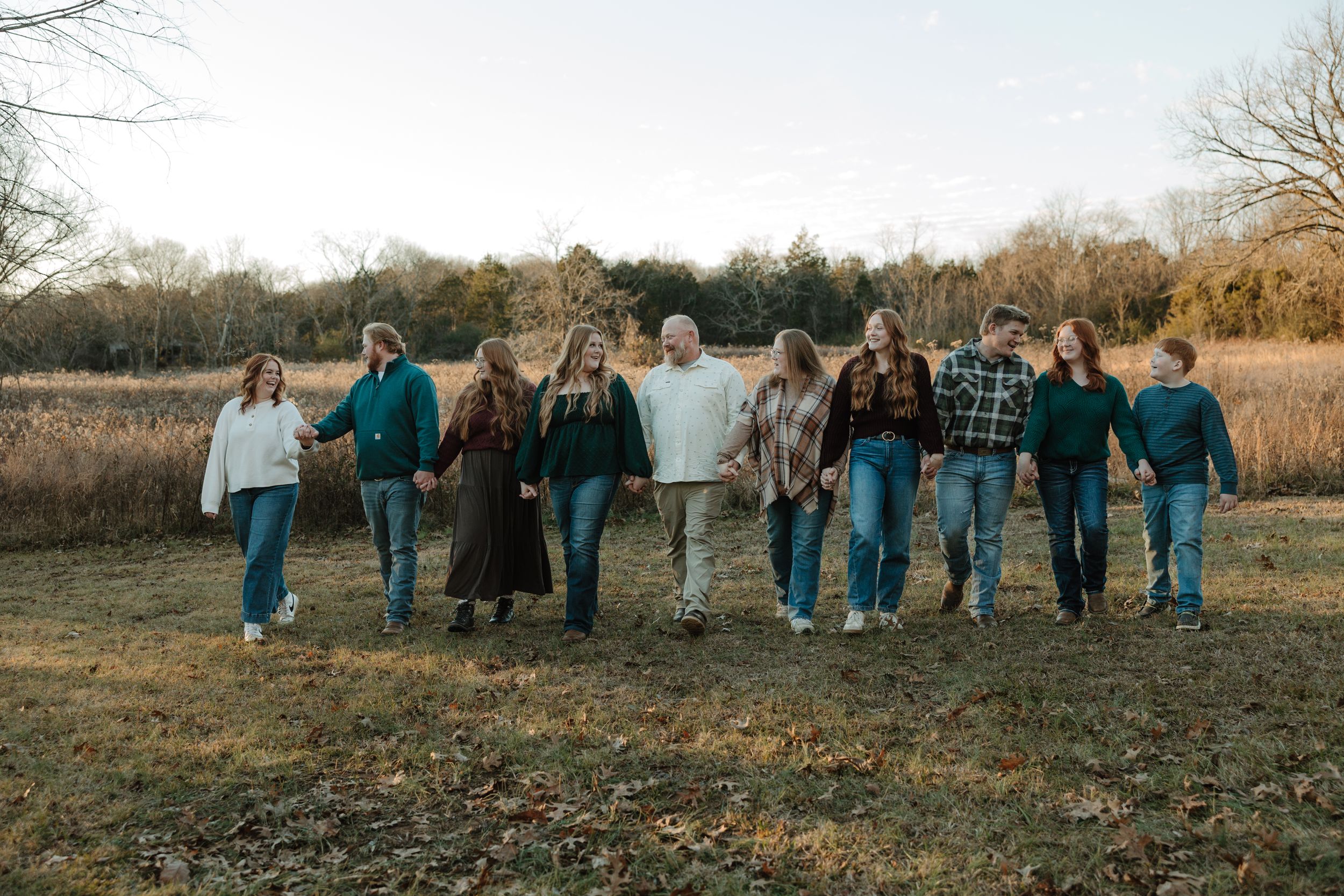 Large family group photo outdoors in a field during autumn, holding a white sign while walking together.