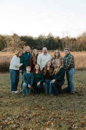 Large family group portrait outdoors in a field wearing coordinated green and blue outfits during a fall photo session.