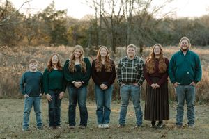 Family of seven posing outdoors in a field during autumn, wearing coordinated green and plaid outfits.