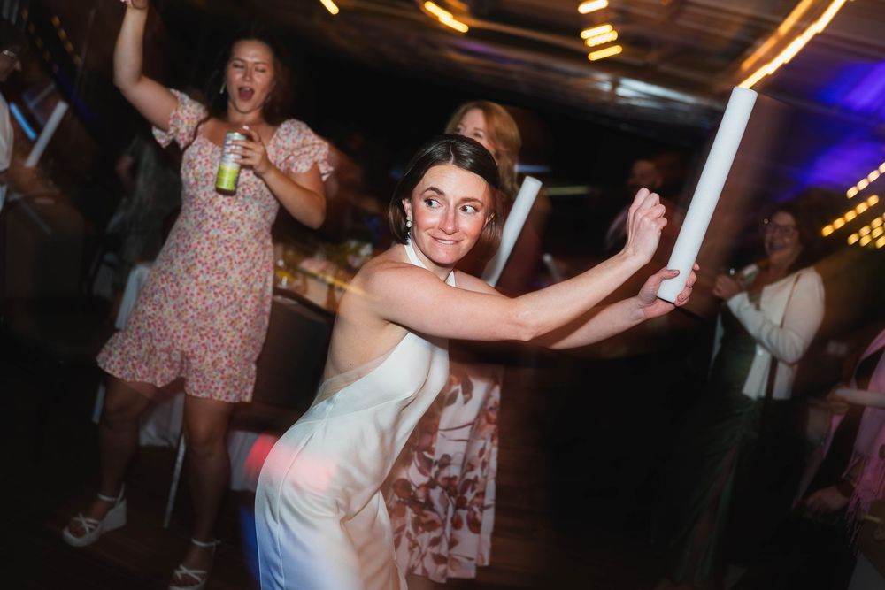 Woman in white dress dancing joyfully at a wedding reception party with friends celebrating in background.