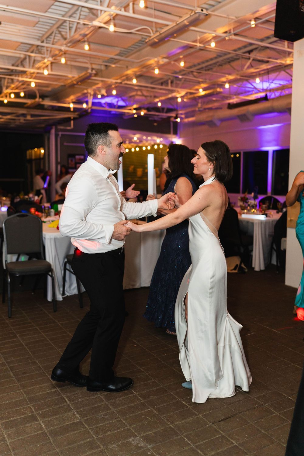 Bride and groom share a joyful dance at their wedding reception under warm string lights.