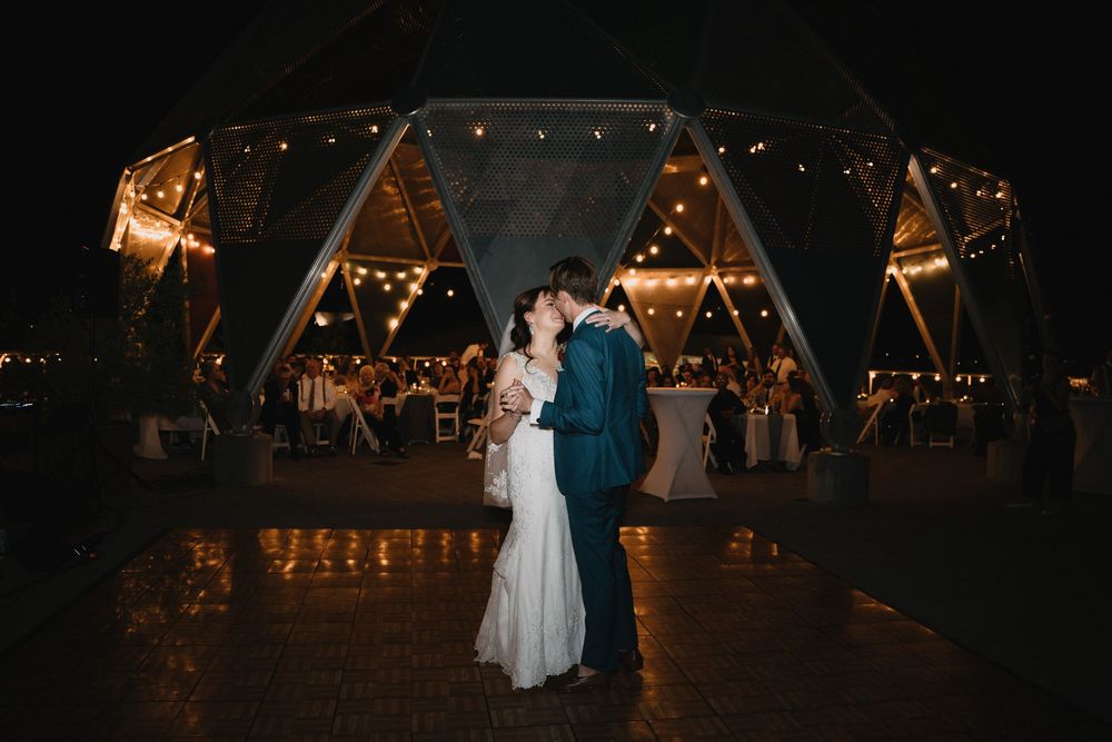 Couple sharing a romantic kiss at night outside a beautifully lit geodesic dome wedding venue.