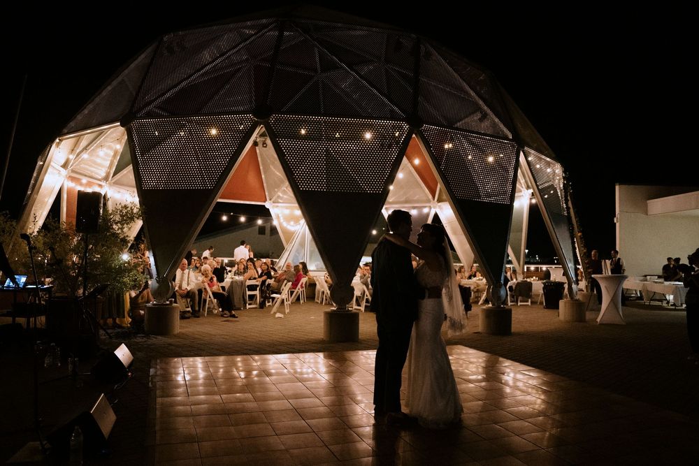 Couple sharing first dance outside illuminated geodesic dome wedding venue at night.