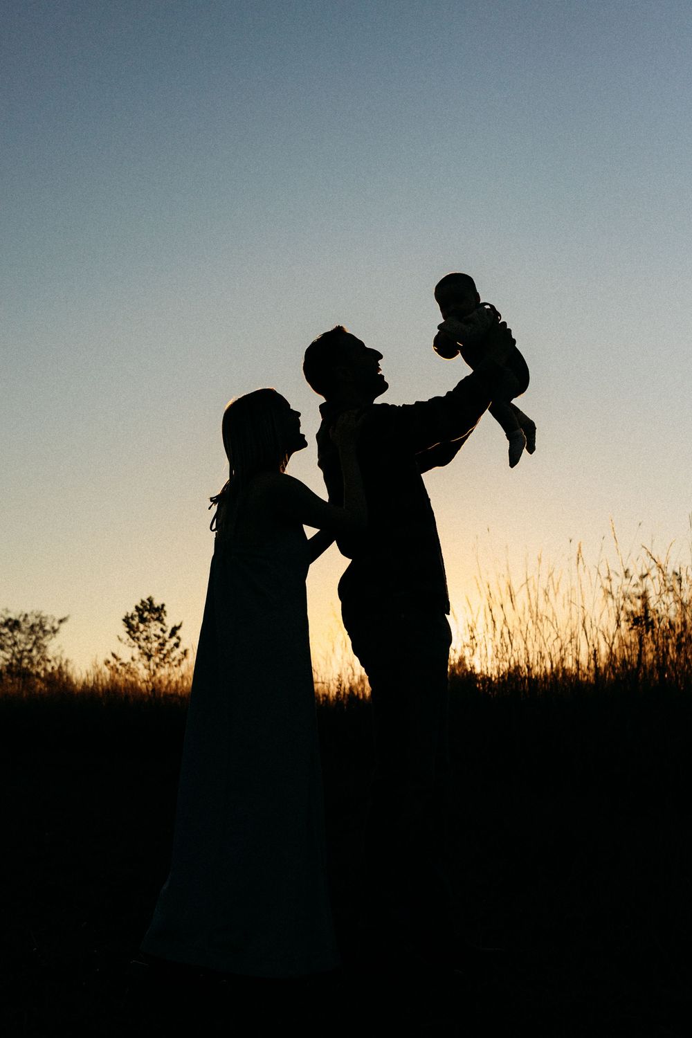 Silhouette of parents lifting baby at sunset in a field, golden hour family portrait.