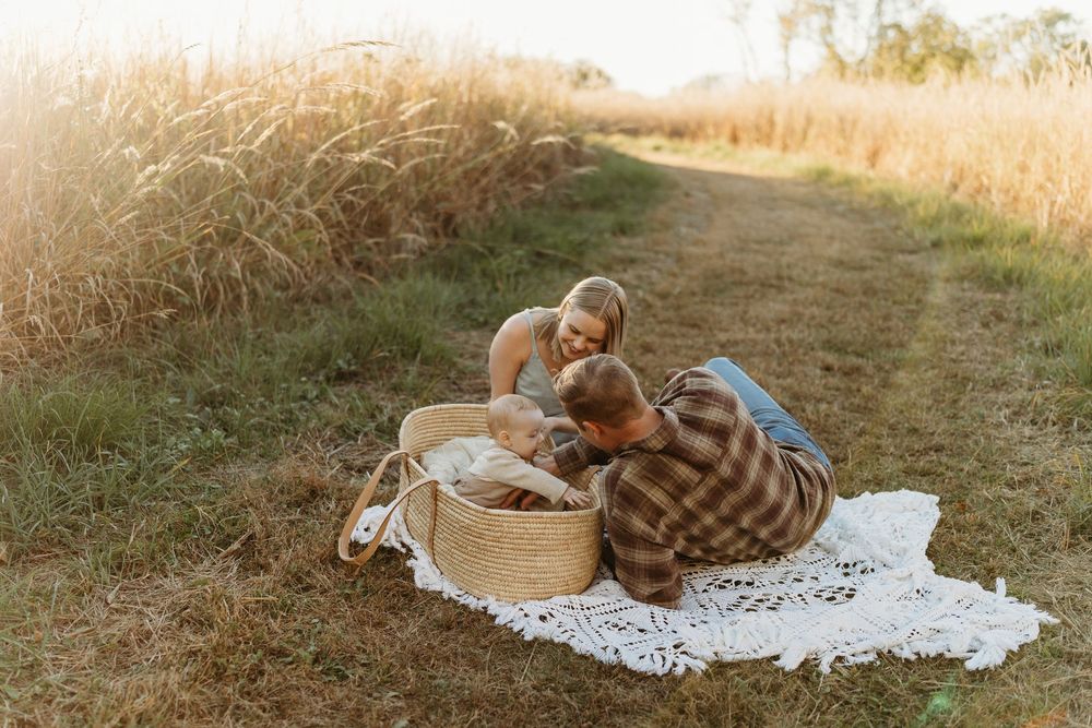 Couple lying on white lace blanket in golden field, looking into wicker basket at sunset.