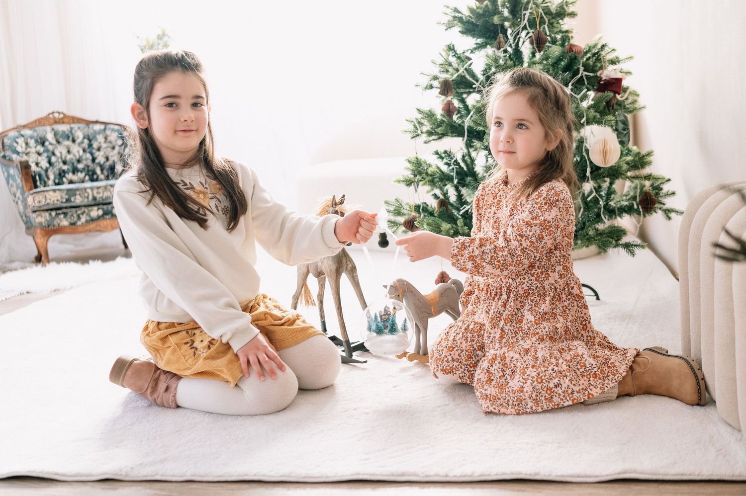 Zwei Mädchen sitzen gemeinsam vor einem geschmückten Weihnachtsbaum und spielen.
